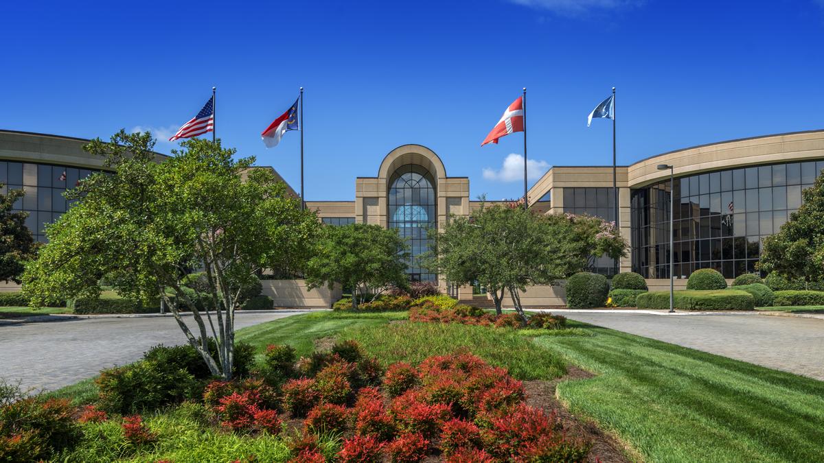 A brown and windowed building with a lush green lawn and four flags waving in the air.