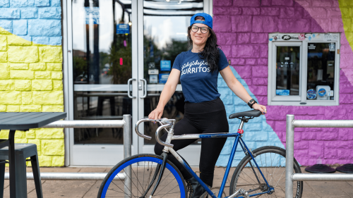 girlsgirlsgirls Burrito's owner and operator Sara Wood holds a blue bike in front of a colorful wall in Lexington, Kentucky