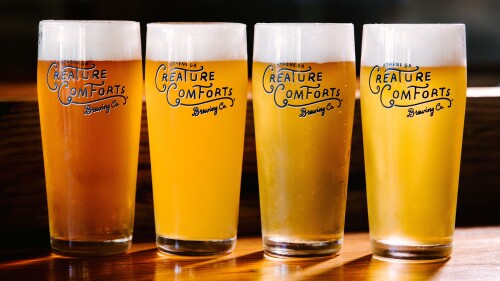 Four pint sized glasses of newly poured draft beer with the logo "Creature Comforts" on each glass