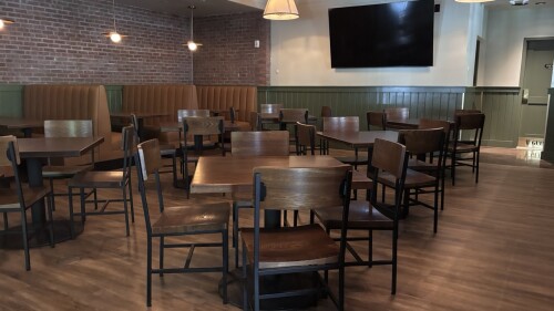 A cozy restaurant dining room with wood floors, wood and black metal tables and brown leather booths.