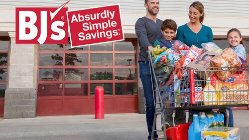 A family stands with a full grocery cart in front of a BJs. 