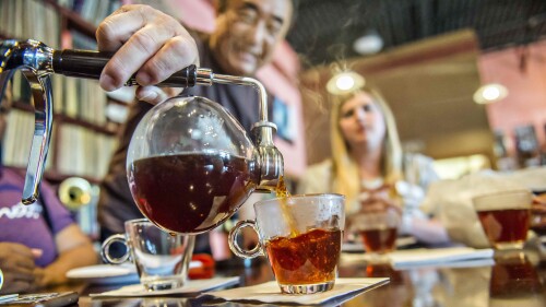 Tea being poured into a glass from a glass pot. 