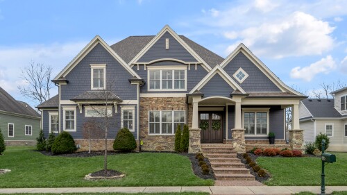 A large, two-story blue house with white trim and stone accents.