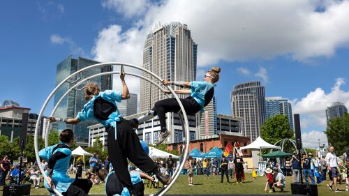 Acrobats demonstrate a live show on a mono-wheel in a park with Uptown Charlotte in the background.