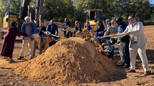 A group of people throwing dirt onto a mound with shovels while smiling. 
