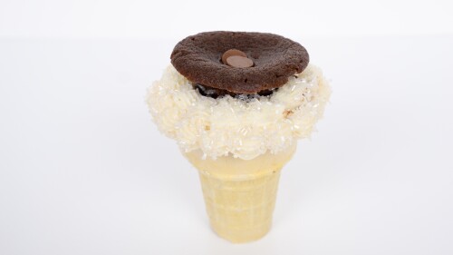 A picture of a cake cone topped with white frosting, sprinkles, and a brownie. 