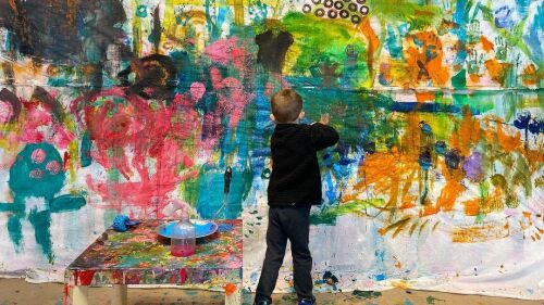 A child paints a canvas hanging on a wall.