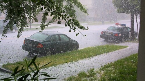 A small car and a police car are parked on a rainy, wet street as hail bombards the road.