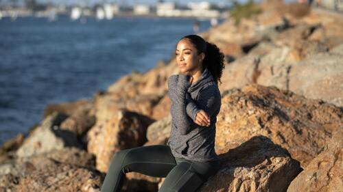 A woman sits on a rock and stretches her arm. 