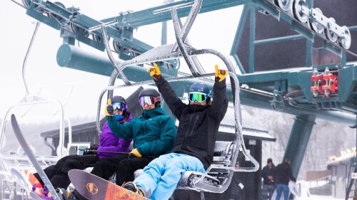 A group of three in snow gear riding a ski lift.