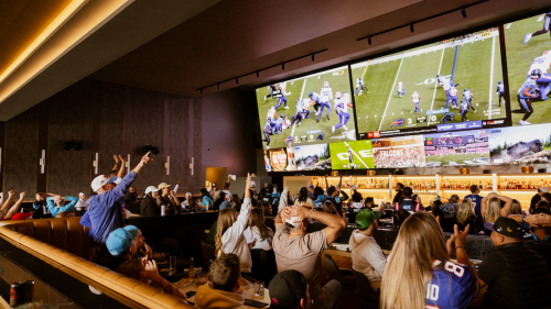 People standing on cheering while watching football on a large screen. 