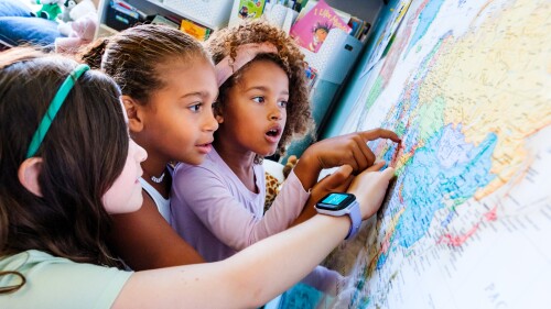 three young children look with curiosity at a map