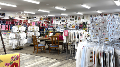 colorful needlepoint supplies hang on shelves around a table and chairs at M's Canvashouse