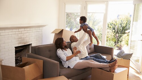 Parents taking a break from packing, playing with their child on a couch. 