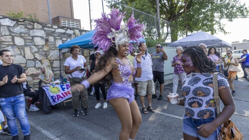 a woman dressed in purple dances and smiles as a crowd looks on
