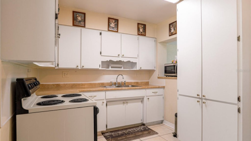 Small kitchen with white cabinets, electric stove, microwave, and beige tile floor and countertops.