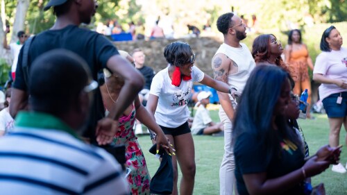 A group of people in a crowd holding hands and watching an unpictured stage performance. 
