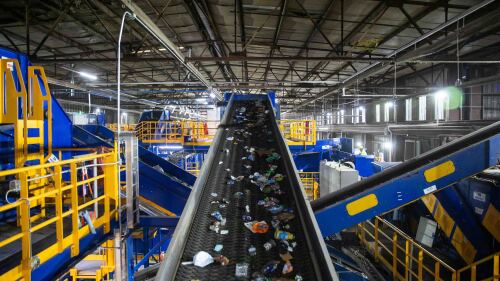 A conveyor belt carries plastic and paper trash through a facility. It crosses other blue and yellow belts.