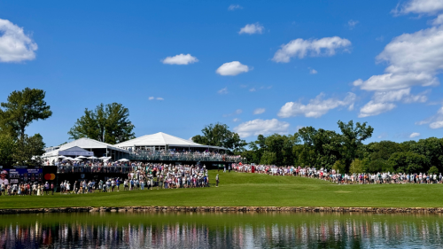 Looking across a pond at Quail Hollow Club, with two white tints and people lining the green course.
