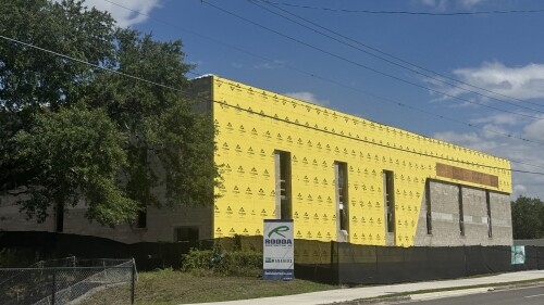 A commercial building under construction with yellow sheathing and a Rodda banner on the sidewalk.