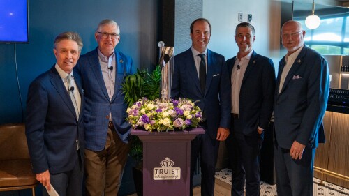 Men in navy blue suit jackets pose for a photo with a silver Truist Championship trophy.