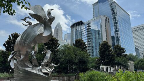 An art sculpture stands in the foreground against the Uptown Charlotte skyline.