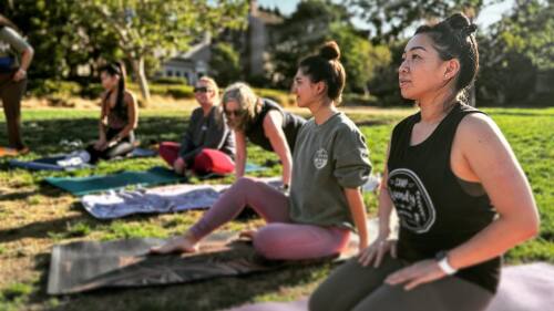 Women sit on yoga mats in a park.