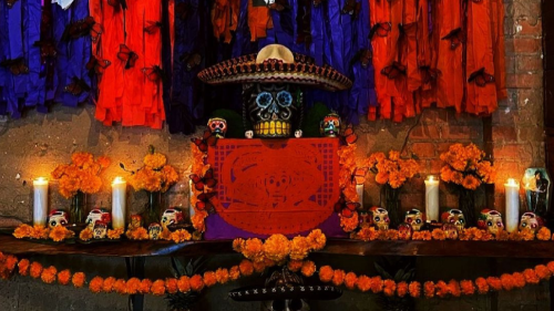 An ofrenda decorated with orange flowers, a skull with a sombrero, and candles.