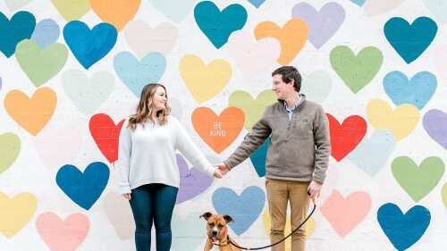 Two people holding hands in front of the Confetti Hearts Wall in South End. 