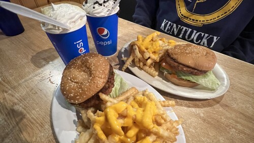 Two plates with burgers and cheese covered fries next to two milkshakes
