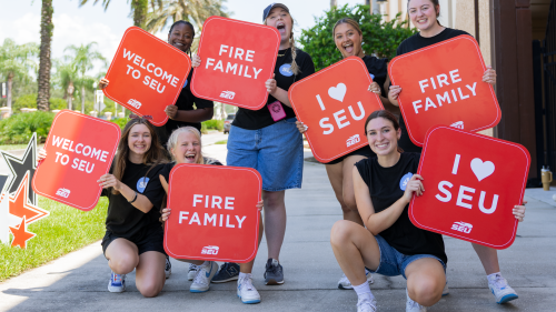 A group of seven southeastern university students hold orange colored signs promoting the university