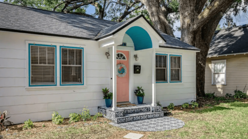 An exterior shot of a white house with a pink door.