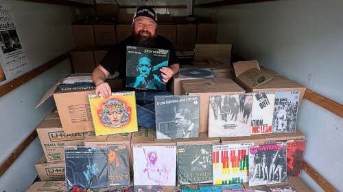 A man posing with records splayed on top of boxes inside of a U-haul.