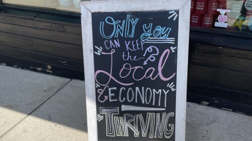 A chalkboard sign from Edge of Urge that says "Only you can keep the local economy thriving."