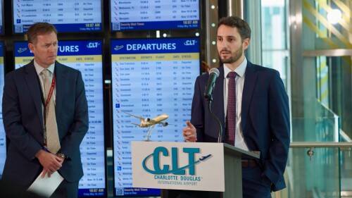 Two suited men stand by a podium at Charlotte Douglas International Airport