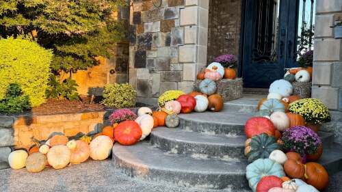 Front porch decorated with colorful pumpkins and mums on stone steps during autumn.