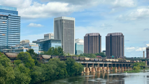 Richmond skline from Belle Isle pedestrial bridge; A train passes over the river, in front of the skyline.