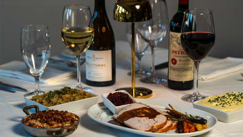 A table with turkey and gravy, glazed carrots, mashed potatoes, and wines.