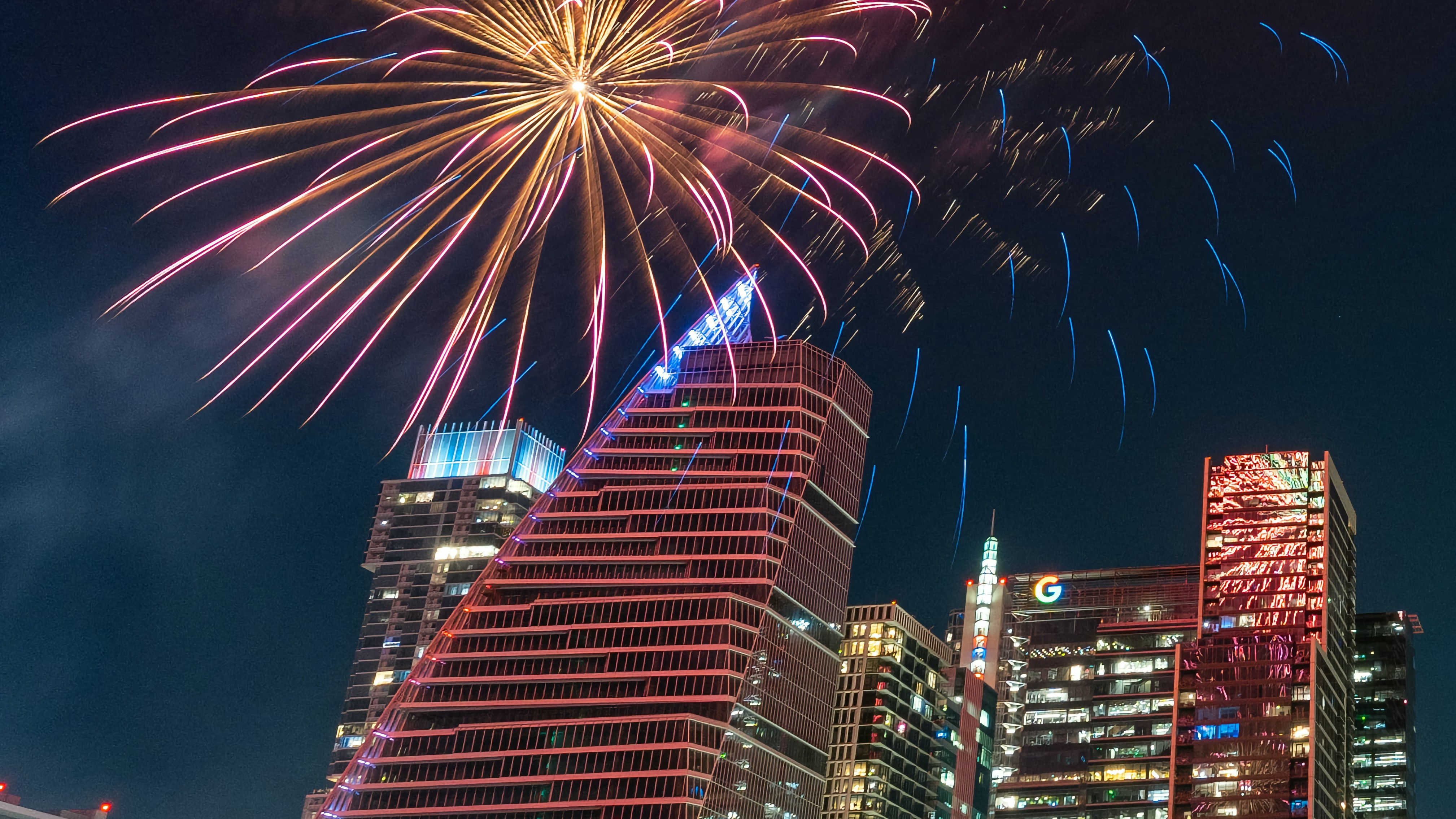 Fireworks exploding over the Google building and other skyscrapers in Downtown Austin.