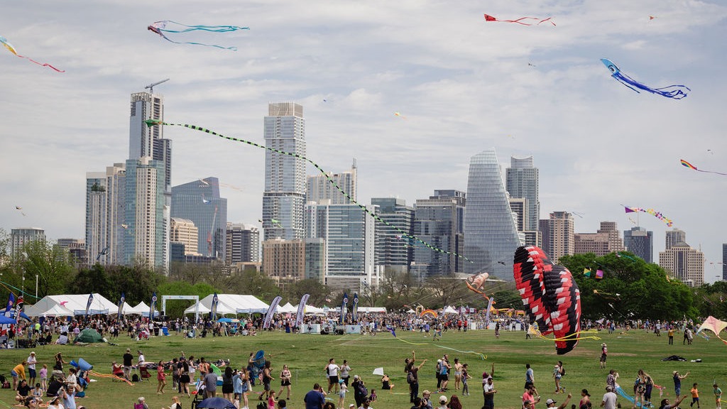 Thousands of people gathered at Zilker Park, flying kites, in front of the Austin Skyline.
