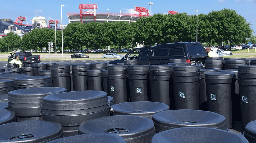 Rain barrels are lined up off the side of a road leading to Nissan Stadium. You can see the stadium in the background.