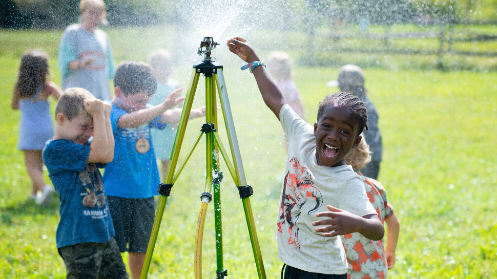Children play joyfully around a sprinkler on a sunny day in a grassy ...