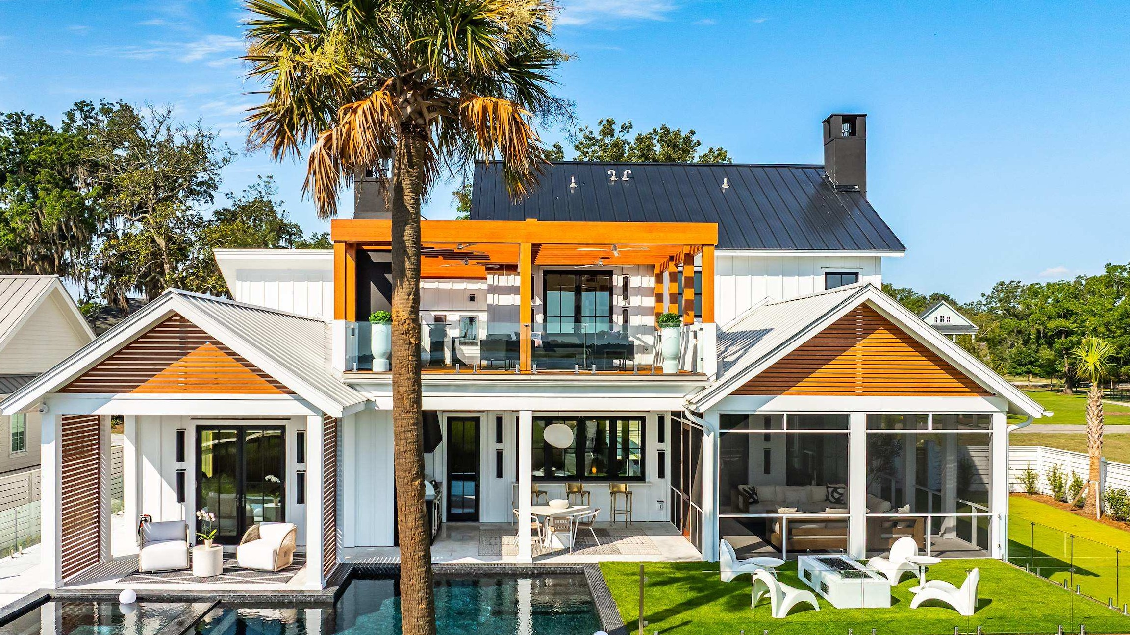 A view of white seaside homes with neat lawns beside salt marshes, tidal channels, and calm water under a bright summer sky.