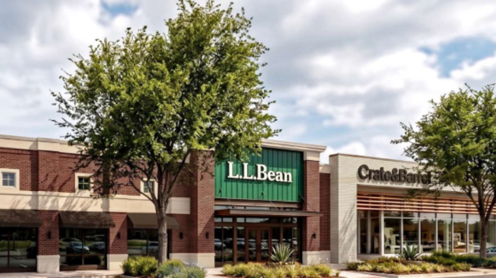 Outdoor shopping center featuring L.L.Bean and Crate & Barrel storefronts, brick architecture, trees, and a bright, partly cloudy sky.